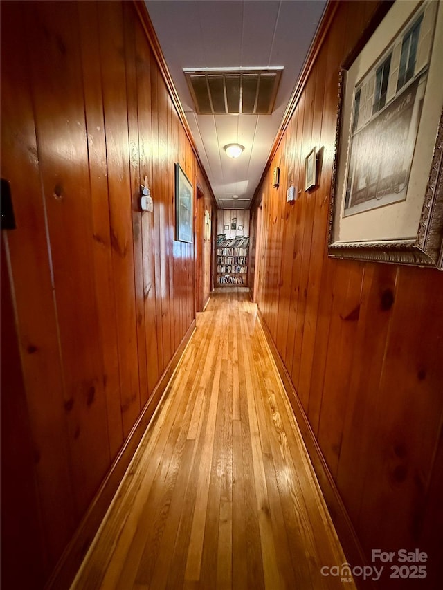 hall featuring light wood-type flooring and wooden walls