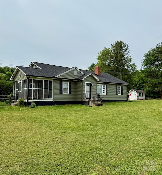 ranch-style house with a sunroom, a front lawn, a chimney, a shingled roof, and an outbuilding