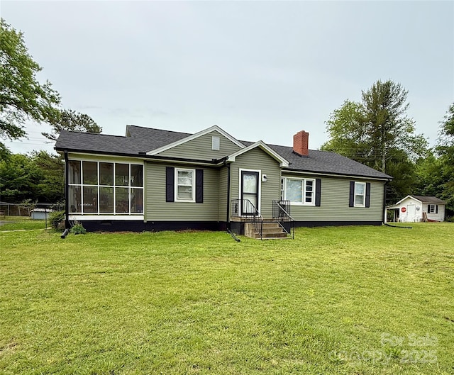 rear view of house featuring a chimney, a lawn, a sunroom, and roof with shingles