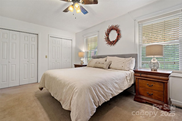 bedroom with two closets, light colored carpet, and a ceiling fan