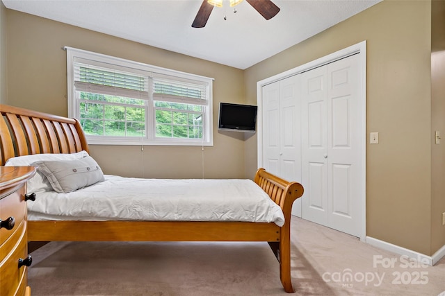 bedroom with a closet, baseboards, light colored carpet, and ceiling fan