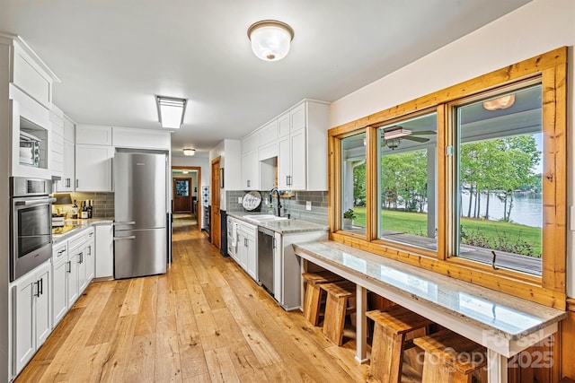 8218 Bright Water Ln, Denver, NC 28037 - kitchen with appliances with stainless steel finishes, a sink, light wood finished floors, white cabinetry, and tasteful backsplash