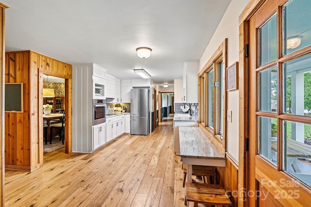 8218 Bright Water Ln, Denver, NC 28037 - kitchen featuring stainless steel appliances, white cabinets, backsplash, light wood finished floors, and wooden walls