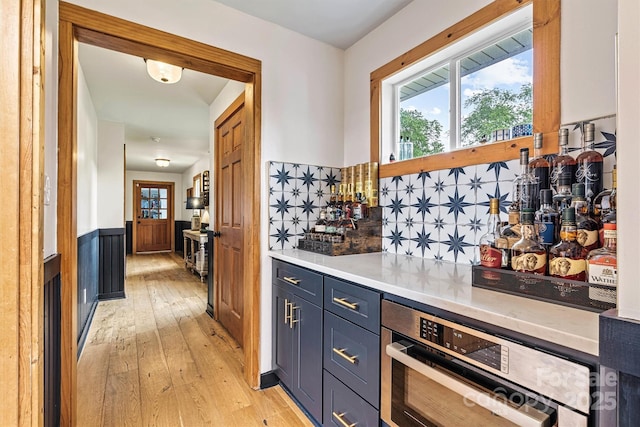 8218 Bright Water Ln, Denver, NC 28037 - bar area with light wood finished floors, healthy amount of natural light, a wainscoted wall, stainless steel oven, and tasteful backsplash