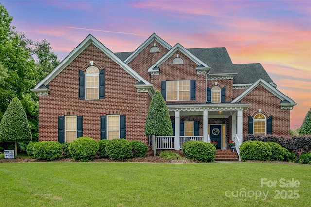 colonial inspired home with brick siding, a yard, a porch, and roof with shingles