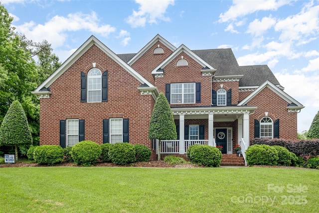 colonial home with brick siding, a front lawn, a porch, and a shingled roof
