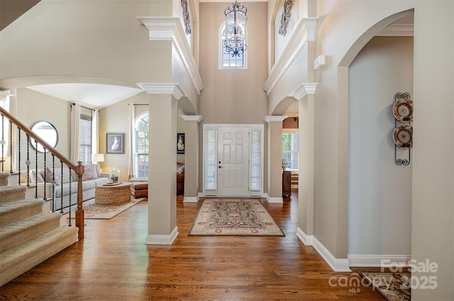 foyer entrance with arched walkways, wood finished floors, stairs, a high ceiling, and a chandelier