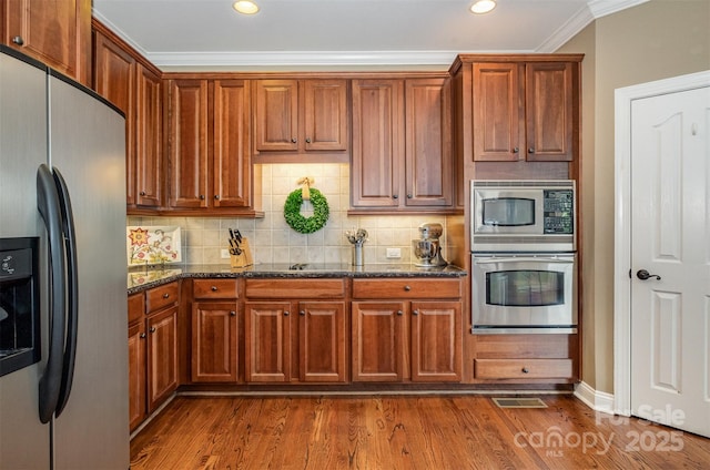 kitchen featuring stainless steel appliances, dark wood-style flooring, ornamental molding, dark stone countertops, and backsplash