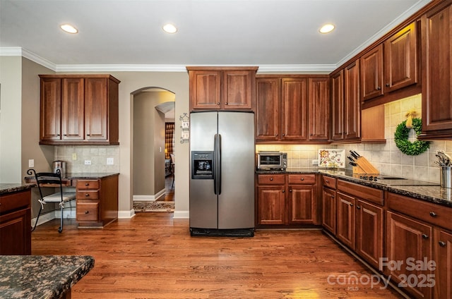 kitchen featuring stainless steel fridge, arched walkways, dark stone countertops, tasteful backsplash, and crown molding
