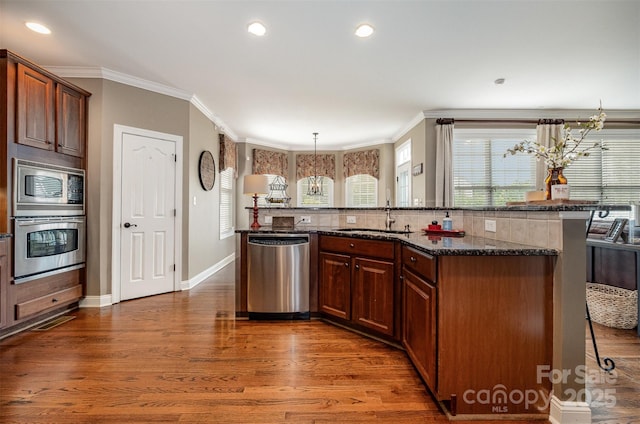 kitchen with appliances with stainless steel finishes, a kitchen breakfast bar, a sink, ornamental molding, and dark wood-type flooring