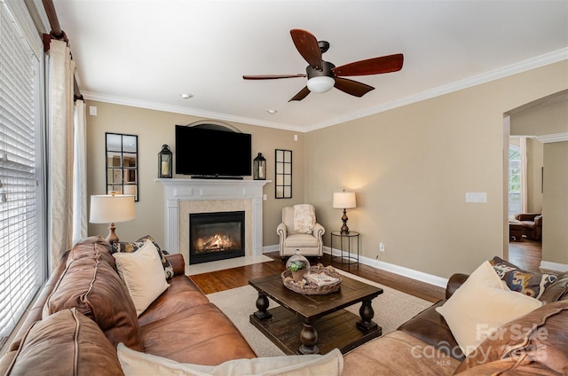 living room with ceiling fan, a fireplace with flush hearth, wood finished floors, crown molding, and baseboards