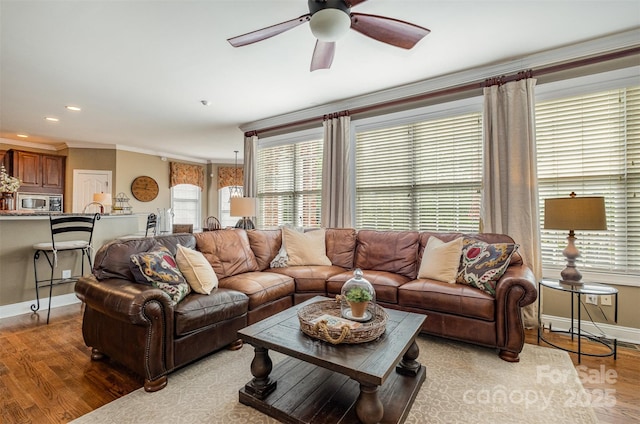 living area with wood finished floors, a ceiling fan, baseboards, crown molding, and healthy amount of natural light