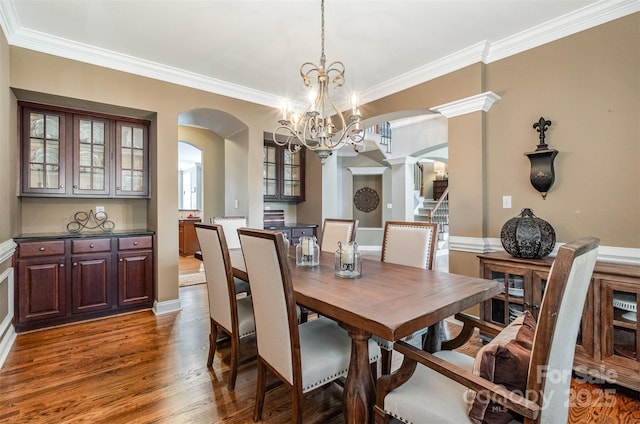 dining room with arched walkways, a chandelier, ornamental molding, wood finished floors, and baseboards