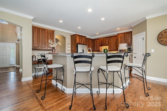 kitchen with freestanding refrigerator, arched walkways, a breakfast bar area, light wood finished floors, and recessed lighting