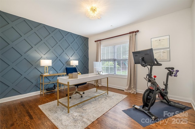 office area with baseboards, a decorative wall, and wood finished floors