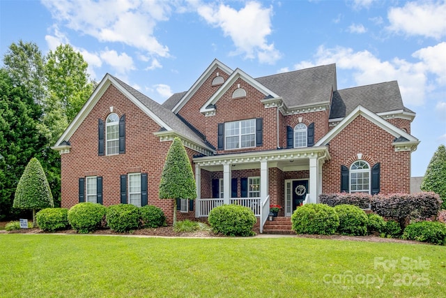 colonial house featuring brick siding, a porch, a front yard, and roof with shingles
