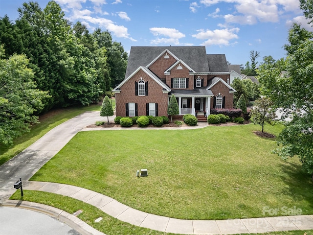 view of front of house featuring a porch, brick siding, concrete driveway, and a front lawn