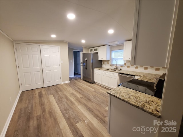kitchen with stainless steel appliances, a sink, light stone counters, white cabinets, and baseboards