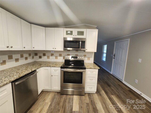 kitchen with appliances with stainless steel finishes, dark wood-type flooring, tasteful backsplash, light stone countertops, and crown molding