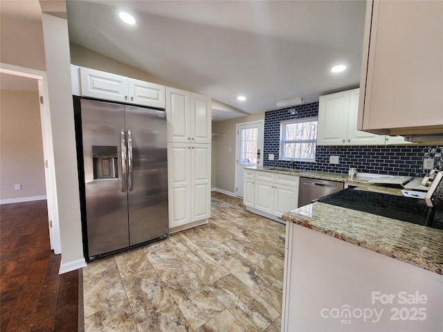 kitchen featuring stainless steel appliances, baseboards, light stone counters, white cabinetry, and vaulted ceiling