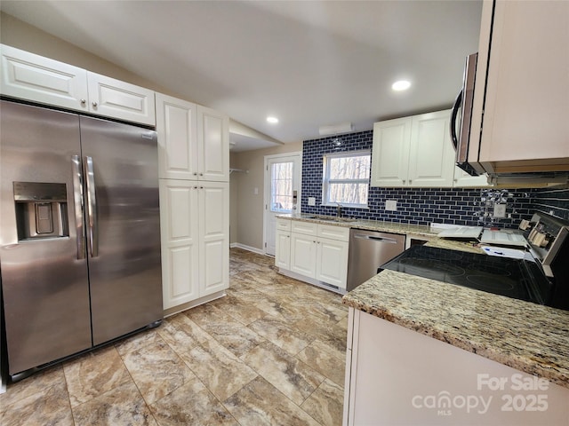 kitchen with appliances with stainless steel finishes, light stone counters, tasteful backsplash, white cabinets, and a sink
