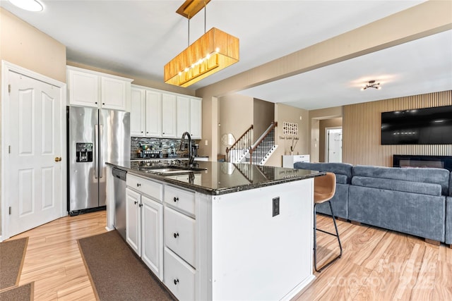 kitchen featuring a sink, stainless steel appliances, white cabinetry, open floor plan, and a kitchen island with sink