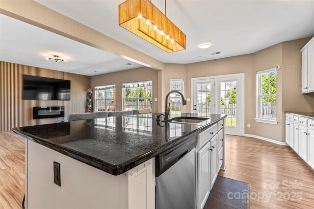 kitchen with stainless steel dishwasher, a sink, light wood-style floors, open floor plan, and a kitchen island with sink