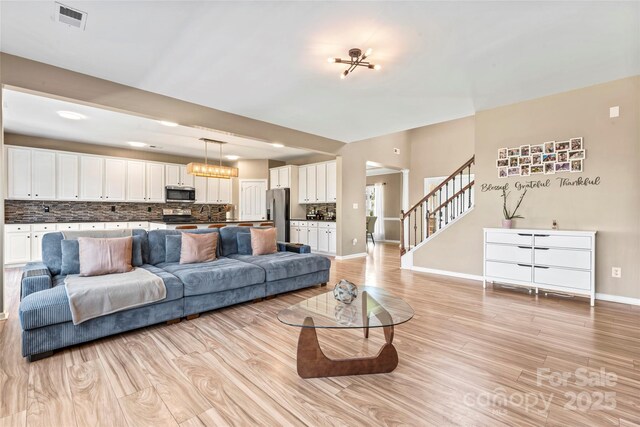 living area with stairs, baseboards, and light wood finished floors