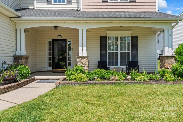 view of exterior entry with covered porch, a shingled roof, and a lawn