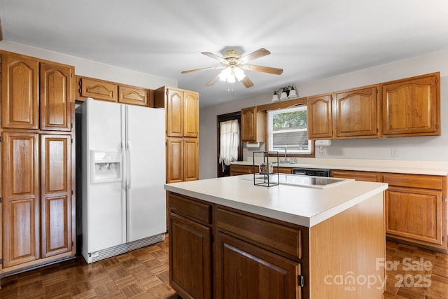 kitchen with white fridge with ice dispenser, a kitchen island, a ceiling fan, light countertops, and brown cabinetry