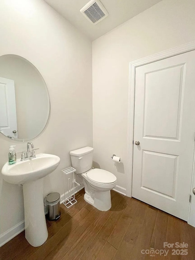 half bathroom with wood finished floors, toilet, and baseboards