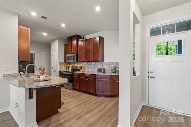 kitchen with stainless steel appliances, light wood-style floors, a sink, light stone countertops, and tasteful backsplash