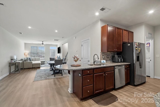 kitchen with stainless steel appliances, a sink, light wood finished floors, tasteful backsplash, and baseboards