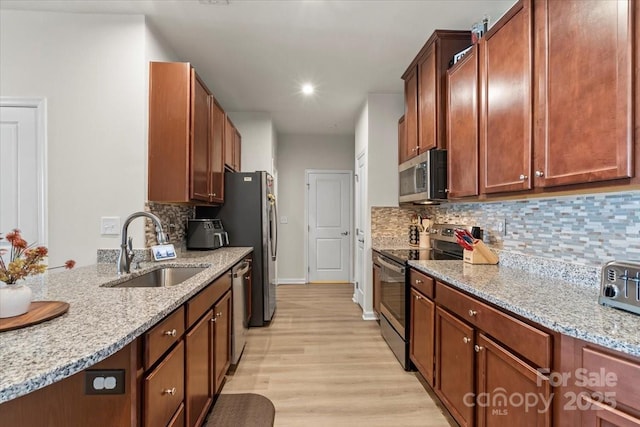 kitchen with appliances with stainless steel finishes, a sink, tasteful backsplash, light wood-type flooring, and light stone counters