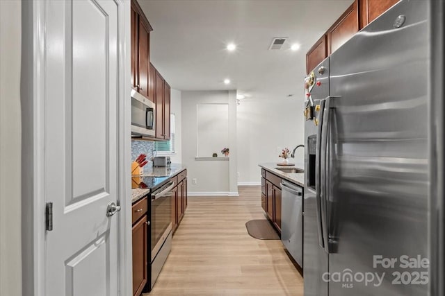 kitchen with appliances with stainless steel finishes, a sink, light wood-style flooring, light stone countertops, and baseboards