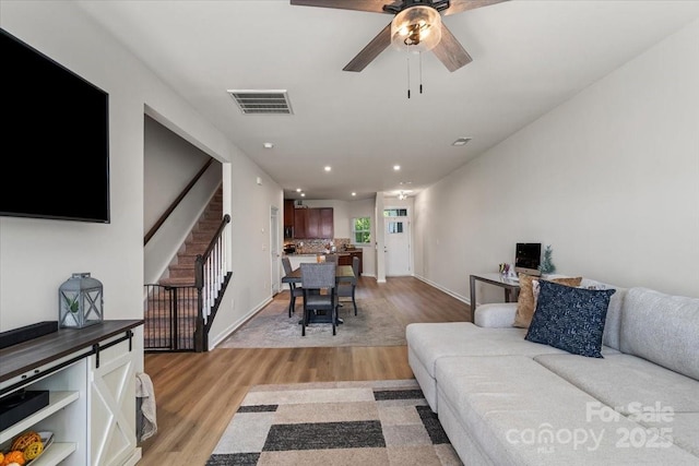 living area with light wood-style flooring, stairs, a ceiling fan, baseboards, and recessed lighting