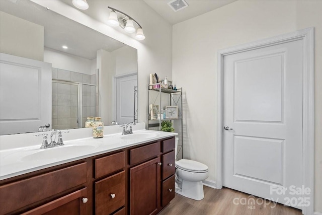 bathroom with a stall shower, wood finished floors, double vanity, and toilet