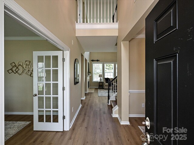 foyer with wood finished floors, baseboards, ornamental molding, and stairway