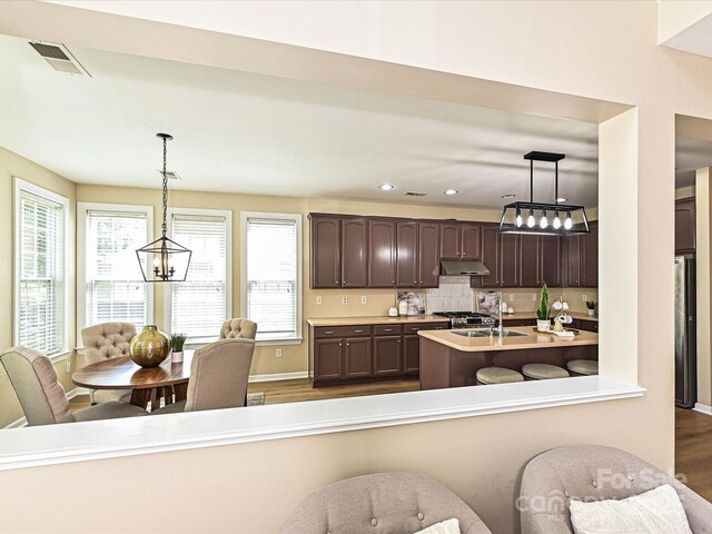 kitchen featuring a chandelier, dark brown cabinets, light countertops, dark wood-style floors, and under cabinet range hood