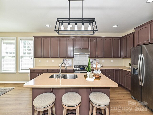 kitchen with stainless steel appliances, a sink, dark brown cabinets, a breakfast bar, and recessed lighting
