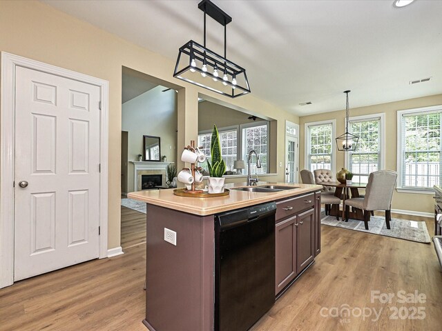 kitchen featuring black dishwasher, a sink, light wood-style floors, light countertops, and dark brown cabinets