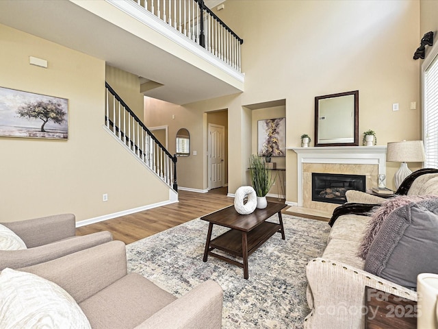 living room with stairway, wood finished floors, a high ceiling, a fireplace, and baseboards