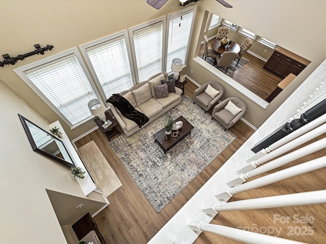 living room featuring wood finished floors, plenty of natural light, a ceiling fan, a towering ceiling, and baseboards