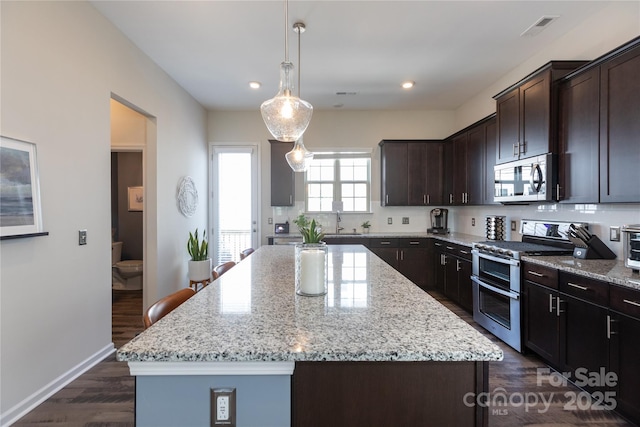 9521 Ainslie Downs St, Charlotte, NC 28273 - kitchen featuring appliances with stainless steel finishes, a center island, light stone counters, dark brown cabinetry, and dark wood finished floors