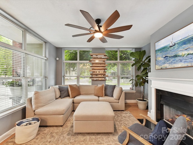 living area with ceiling fan, wood finished floors, a glass covered fireplace, and baseboards