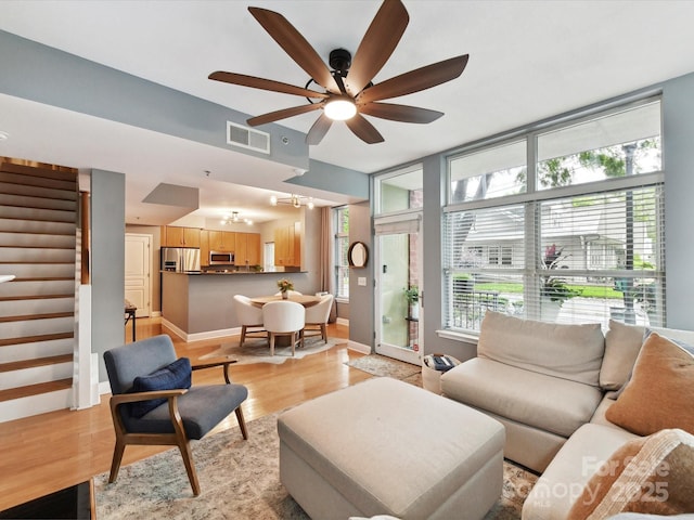 living area with stairway, light wood-type flooring, a ceiling fan, a chandelier, and baseboards