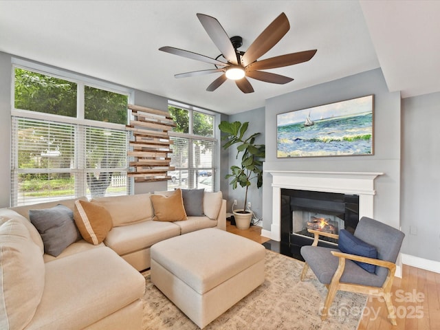 living area featuring a ceiling fan, baseboards, a fireplace with flush hearth, and wood finished floors