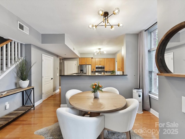 dining area with a chandelier, light wood-type flooring, stairs, and baseboards