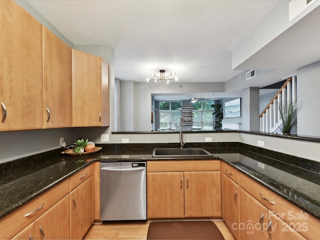 kitchen featuring dishwasher, a sink, dark stone counters, light wood finished floors, and a chandelier