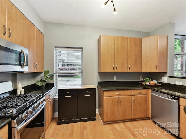 kitchen featuring appliances with stainless steel finishes, light wood-type flooring, and dark stone countertops